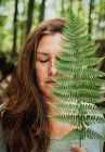 Portrait of woman with eyes closed covering face with fern leaf. — Stock Photo