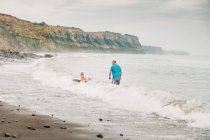 Vater und sohn boogie boarding am strand — Stockfoto