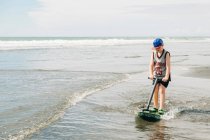 Giovane ragazzo che gioca sulla spiaggia in acqua con il suo skim board — Foto stock