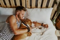 Um jovem loiro dormindo ao lado de seu cachorro na cama. Conceito de estilo de vida — Fotografia de Stock