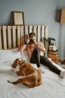 Ein kleiner blonder Junge fotografiert seinen Hund im Bett. Lifestyle-Konzept — Stockfoto
