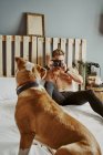 A young blond boy taking pictures of his dog in bed. Lifestyle concept — Stock Photo