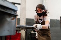 Female blacksmith in protective mask in workshop doing metal work — Stock Photo