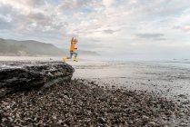 Young curly haired child leaping from a rock at the beach in New Zealand — Stock Photo