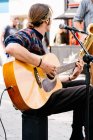 Вертикальное фото избирательного фокуса на руках молодого человека, играющего на гитаре на переполненной улице — стоковое фото