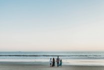 Young family standing on beach holding hands looking out at the ocean — Stock Photo