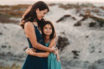 Beautiful 45 yr old mom embracing young daughter at the beach — Stock Photo