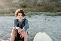 Довговолосий підліток сидить біля серфінгу на пляжі в Новій Зеландії. — стокове фото