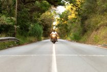 Jovem em uma motocicleta vintage em uma estrada de montanha ao pôr do sol — Fotografia de Stock