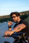 Модний молодий чоловік сидить і курить на класичному мотоциклі на заході сонця . — стокове фото