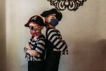 Hermanos en edad escolar vestidos de piratas con mascarillas en casa - foto de stock