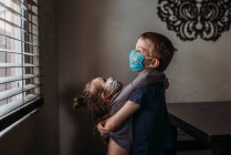 Lifestyle portrait of young siblings with masks on hugging at home — Stock Photo