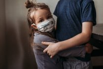 Close up of young girl with mask on being hugged by big brother — Stock Photo