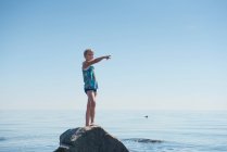Chica joven de pie en la roca por el océano - foto de stock