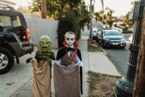 Jeunes frères et sœurs habillés en costumes d'Halloween pendant Trick-or-Treat — Photo de stock