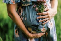 Tiro recortado de la mujer embarazada sosteniendo flores por el vientre - foto de stock