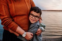Happy young boy hugging mom near a lake on a autumn evening — Stock Photo