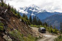 Сучасний автомобіль їде по нерівній лісовій дорозі біля нерівного схилу під час подорожі через сніжні гори у Британській Колумбії (Канада). — стокове фото