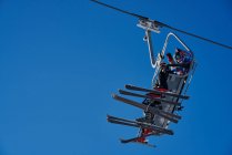 Лыжники на подъемнике смотрят вниз на синем фоне — стоковое фото