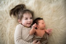 Grande sorella abbraccia neonato fratello mentre posa su fuzzy tappeto — Foto stock