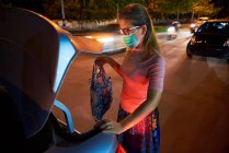 Жінка поклала свою приналежність до багажника автомобіля після покупок під час COVID — стокове фото