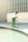 Portrait extérieur de beau jeune homme avec téléphone portable et vélo à engrenages fixes dans la rue. — Photo de stock