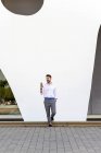 Junger bärtiger Mann lehnt mit dem Handy an einer weißen Wand — Stockfoto