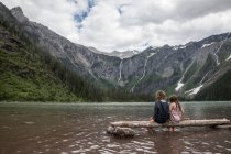 Children sitting on wood in the mountain lake — Stock Photo