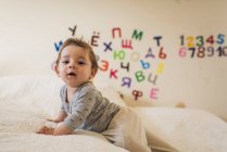 Baby crawling on white bedspread with letters and numbers on wall — Stock Photo