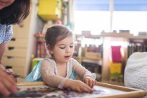 4 anos de idade menina trabalhando em um quebra-cabeça na sala de jogos com a ajuda da mãe — Fotografia de Stock