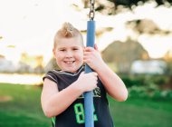 Молодий хлопчик грає на гойдалках у парку на заході сонця — стокове фото