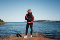 Женщина стоит на скале с рюкзаком, глядя на океан и острова — стоковое фото