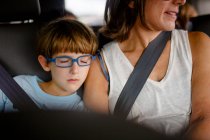 Un petit enfant avec des lunettes bleues dort sur l'épaule de sa mère dans la voiture — Photo de stock