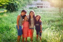 Happy children stand with arms around each other in sunlit field — Stock Photo