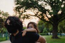 Pai dando filha um passeio de piggyback, ambos vestindo máscaras — Fotografia de Stock