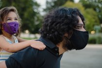 Kleines Mädchen reitet huckepack mit ihrem Vater mit Gesichtsmasken — Stockfoto