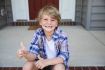 Desdentado primeiro grau menino dá polegares para cima enquanto sentado no tijolo passos — Fotografia de Stock