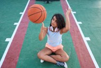 Маленькая девочка, сидящая за столом, крутит баскетбольный мяч. Концепция образа жизни — стоковое фото