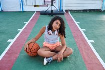 Una chica sentada con una pelota de baloncesto frente a la cámara, concepto de estilo de vida - foto de stock