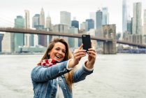 Привлекательная женщина, использующая смартфон с Нью-Йоркским горизонтом на заднем плане — стоковое фото