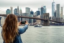 Atractiva mujer usando su teléfono inteligente con el horizonte de Nueva York en el fondo - foto de stock