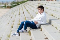 Side view of young man sitting on outdoors staircase, looking away — Stock Photo