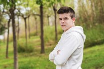 Side view young man standing outdoors while looking camera arms crossed — Stock Photo