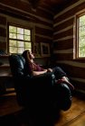 Woman resting in leather recliner chair in a rustic log cabin home. — Stock Photo