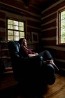 Mujer descansando en silla reclinable de cuero en una casa de cabaña de madera rústica. - foto de stock