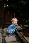 Niño de dos años en pijama agachado en el patio delantero debajo de Grapevine - foto de stock