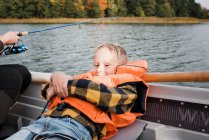 Young boy sat relaxing on a boat whilst out on a boat fishing — Stock Photo