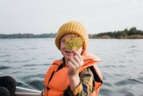 Kleiner Junge auf einem Fischerboot hält ein Ahornblatt in die Höhe und sieht glücklich aus — Stockfoto