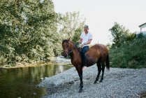 Portrait d'un jeune homme blond chevauchant un cheval sur une rivière — Photo de stock