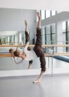 Giovane donna, ballerina professionista in prova abbigliamento facendo arabescue vicino sbarre in studio di coreografia — Foto stock
